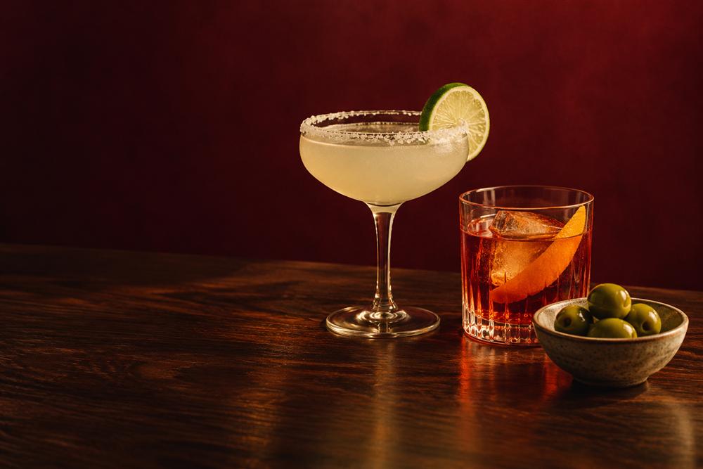 A margarita and a Negroni beside a bowl of olives on a wooden bar